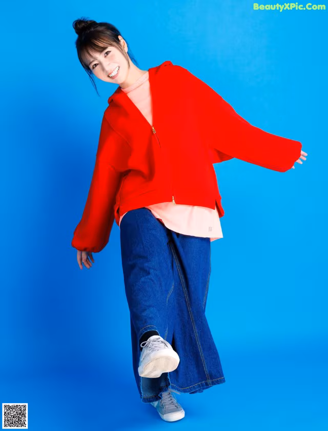 A woman in a red jacket and blue jeans posing for a picture.