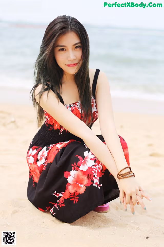 A woman sitting on the beach in a red and black dress.