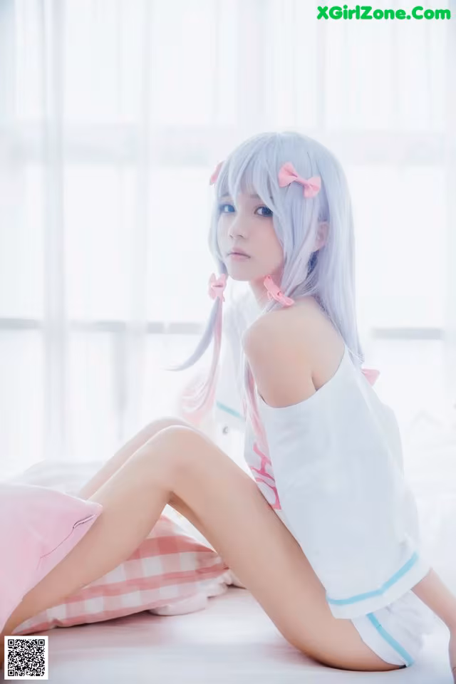 A woman sitting on a bed with a pink pillow.