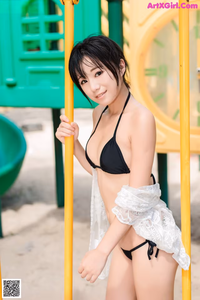 A woman in a black bikini posing on a playground.