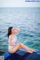 A woman in a white bathing suit sitting on the edge of a swimming pool.