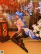 A woman with blue hair sitting on the floor in front of flowers.