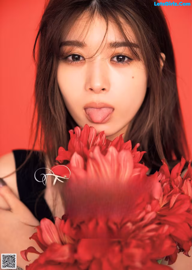 A woman holding a bunch of red flowers in front of her face.