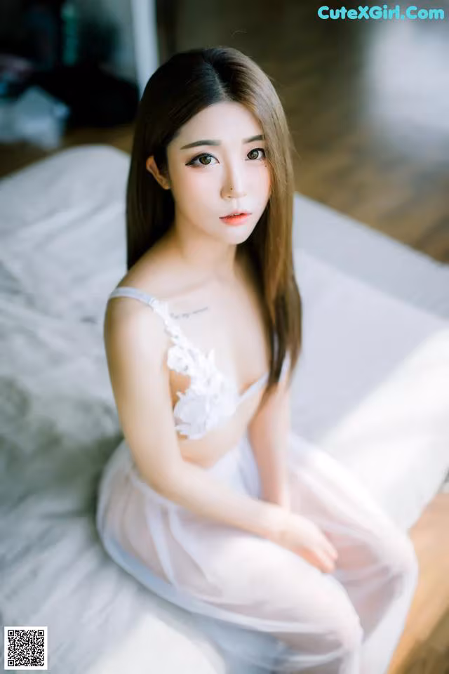 A woman in a white dress sitting on a bed.